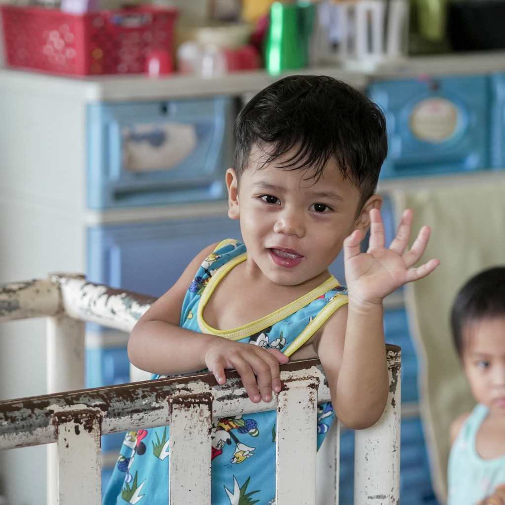 Young child waving from behind a metal railing.