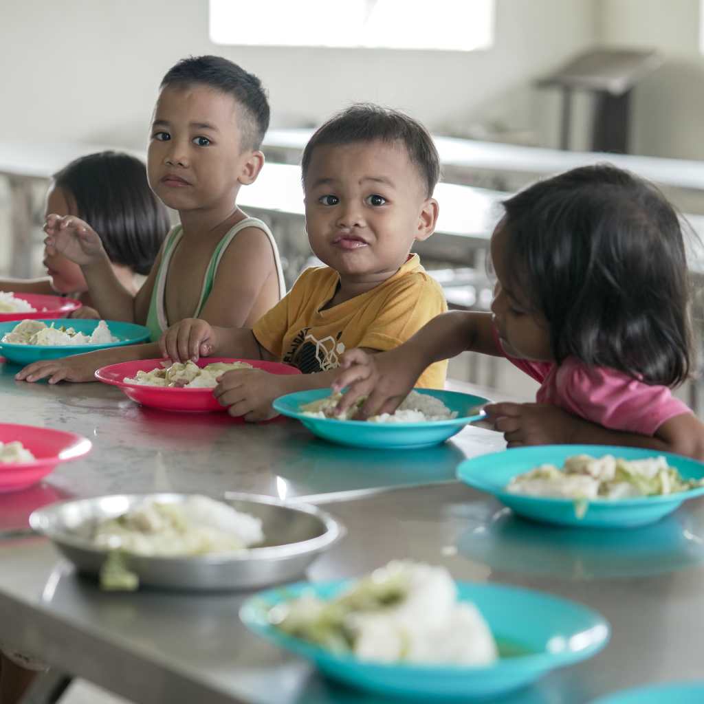 Children seated along a long table with plates of food in front of them.
