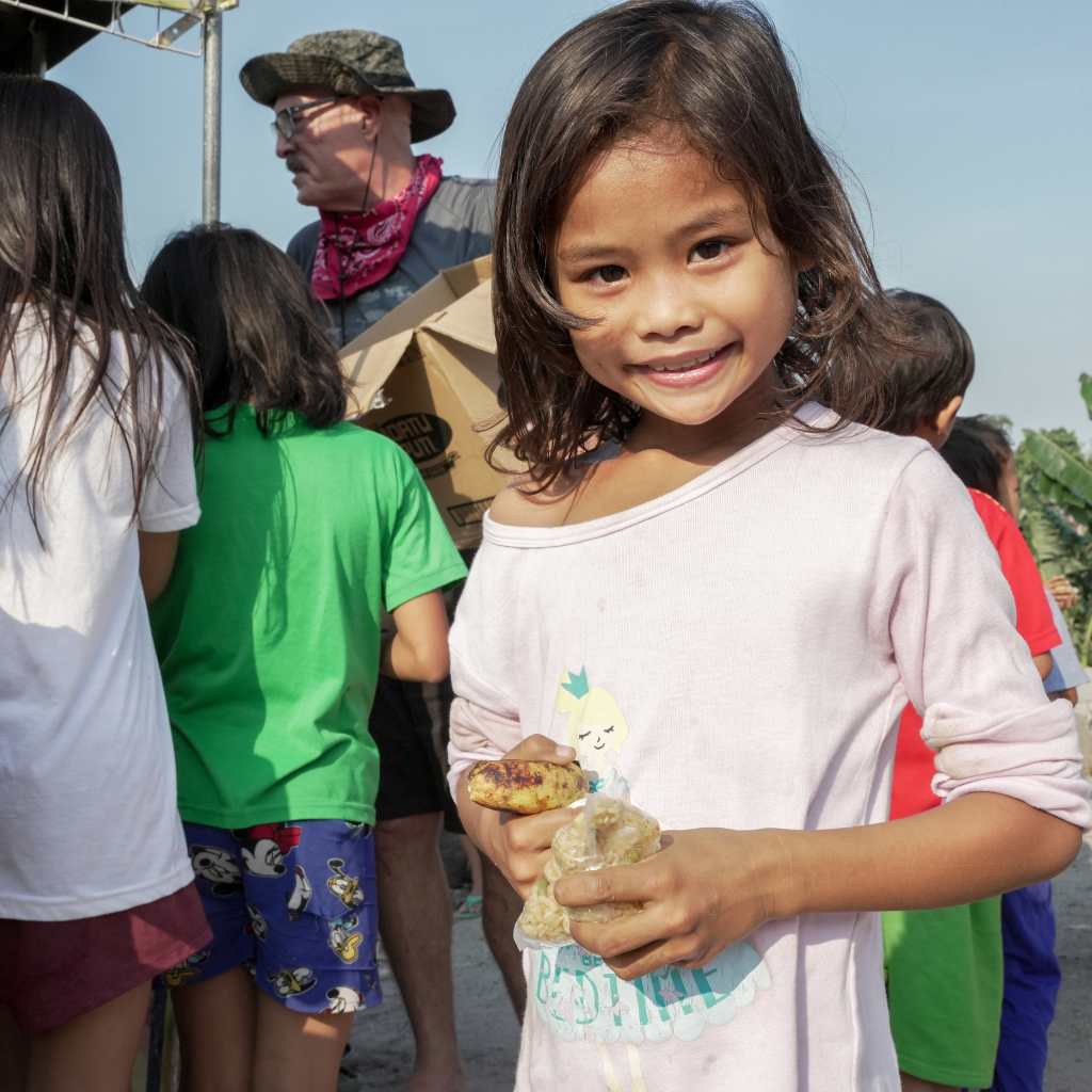 Smiling young girl outdoors holding a small item in her hands.