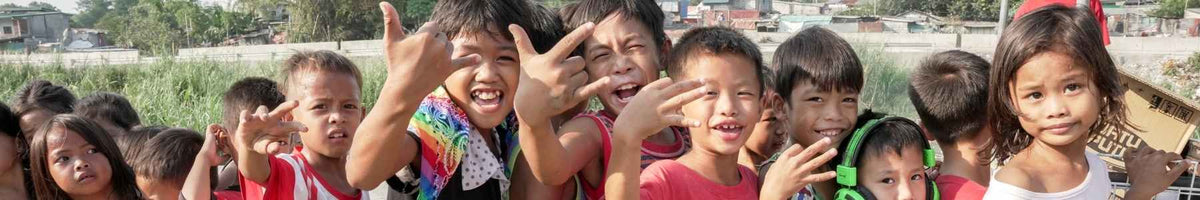 Wide banner of children outdoors smiling and waving towards the camera.
