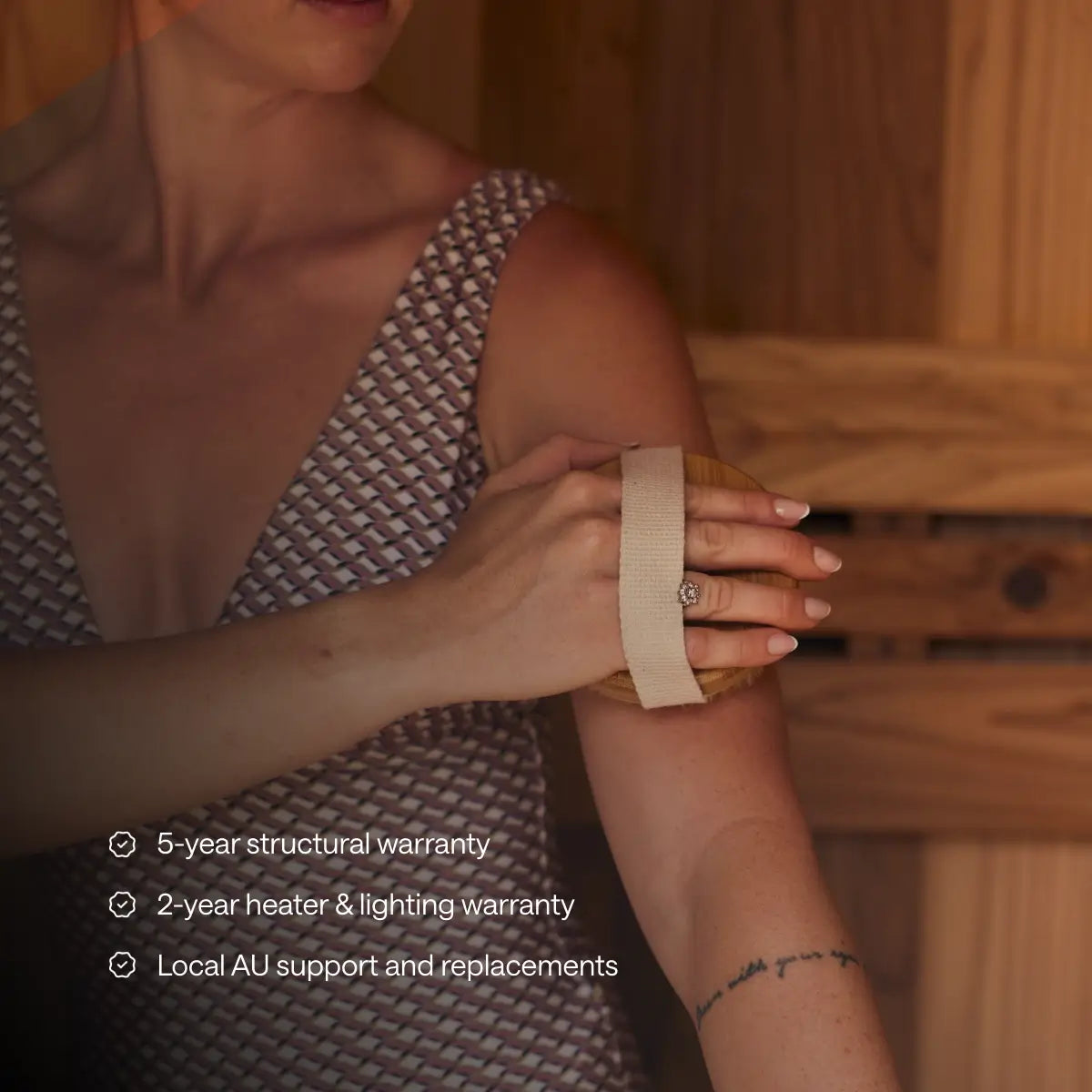 A woman uses a body brush inside a Kiva Wellness Ritual sauna beside warranty and support information.