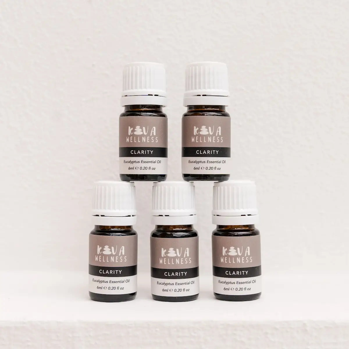 Five Kiva Wellness Clarity eucalyptus essential oil bottles with white caps displayed on a pale pedestal.