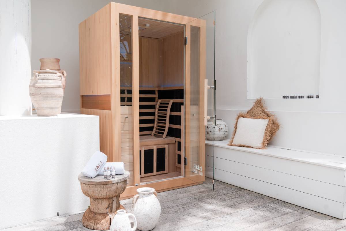 Timber Kiva Wellness sauna beside a white bathtub, woven baskets and rolled towels in a bright bathroom.