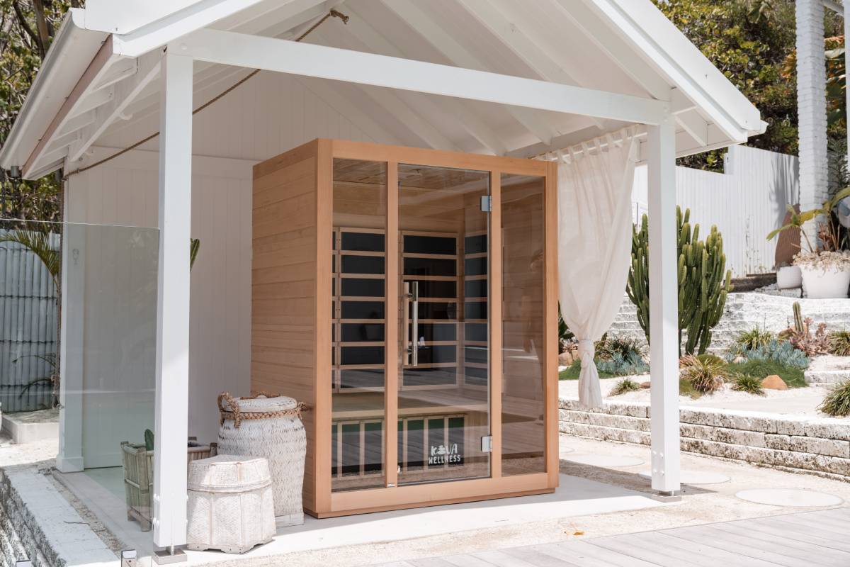 Timber Kiva Wellness sauna sheltered beneath a white garden pavilion beside stacked towels.