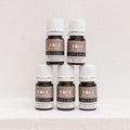 Five Kiva Wellness Earth & Wood frankincense essential oil bottles with white caps on a pale pedestal.