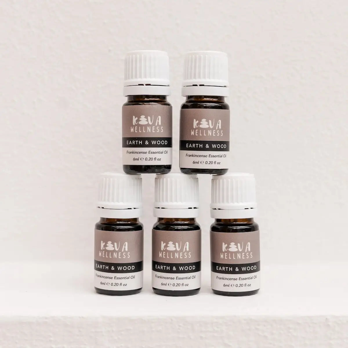 Five Kiva Wellness Earth & Wood frankincense essential oil bottles with white caps on a pale pedestal.