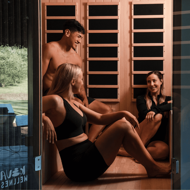 A man and two women sitting together inside a timber Kiva Wellness sauna.