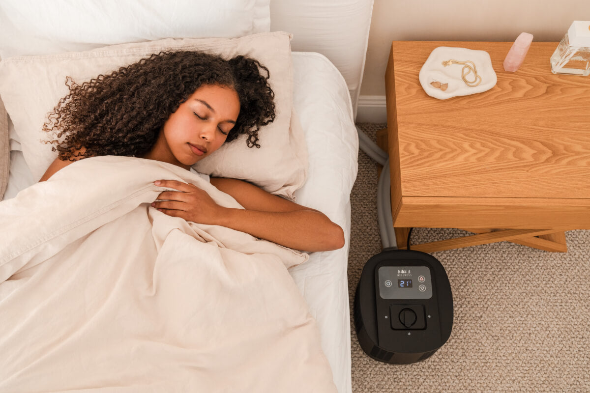 Woman sleeping under pale bedding with a black sleep cooling unit beside the bed.