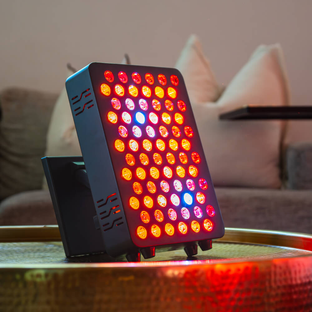 Kiva Wellness Solace Glow red light therapy panel illuminated on a low table beside a sofa.