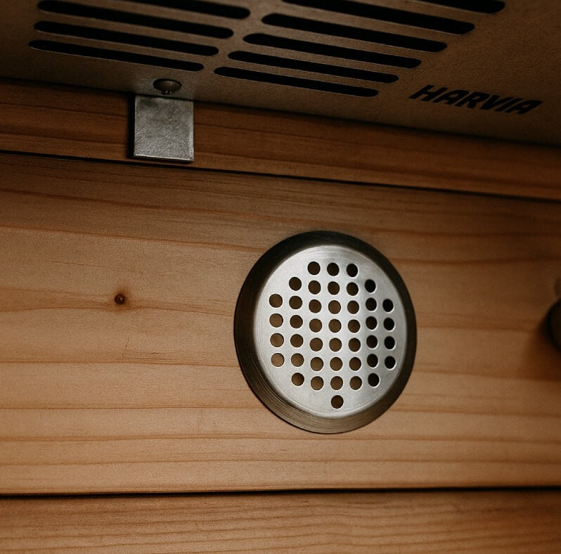 Circular metal ventilation grille in a timber sauna wall beneath a Harvia heater.
