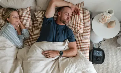 Overhead view of a couple sleeping beside a bedside table with a Circadian Sleep Pod unit on the floor.
