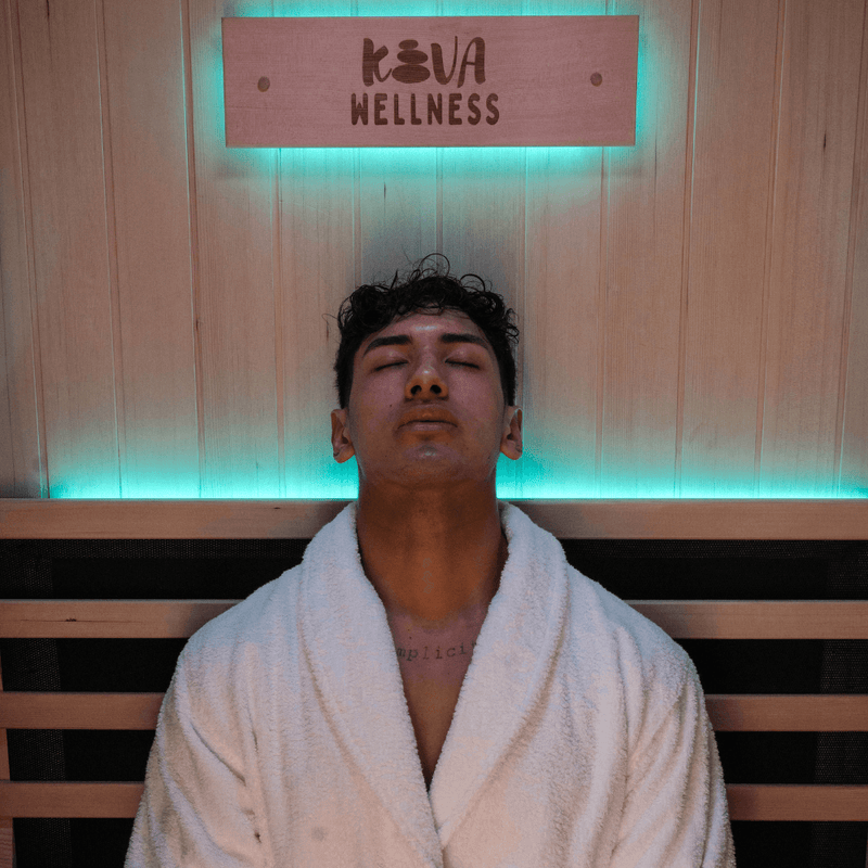 Man in a white robe sitting with his eyes closed beneath a Kiva Wellness sign and blue lighting.