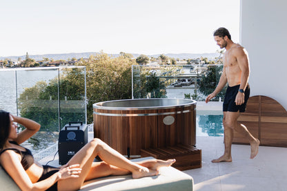 Two people by a ice bath on a patio with a scenic view.