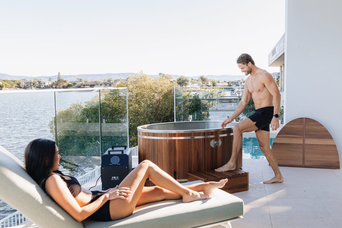Two people by a hot tub on a balcony with a view of water and trees.
