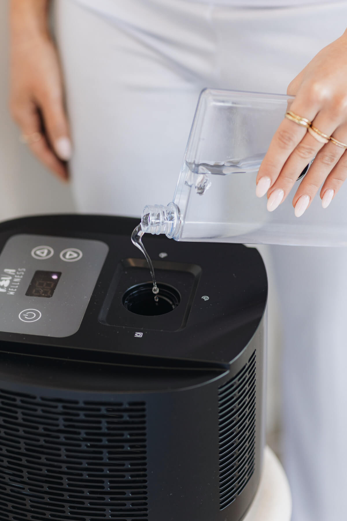 Person pouring water from a clear jug into the top reservoir of a black sleep cooling unit.