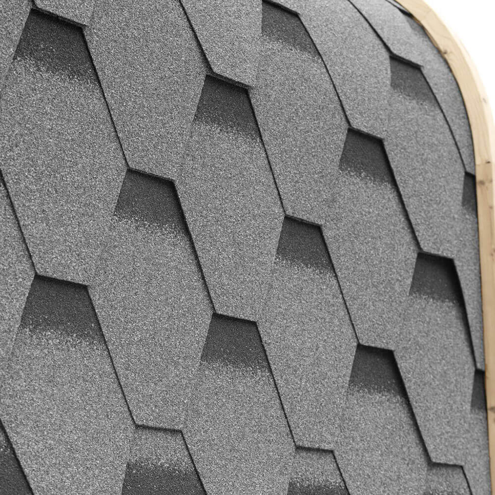 Close view of overlapping dark bitumen roof shingles along the curved edge of an outdoor sauna.
