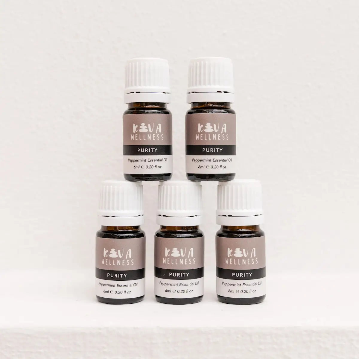 Five Kiva Wellness Purity peppermint essential oil bottles with white caps displayed on a pale pedestal.