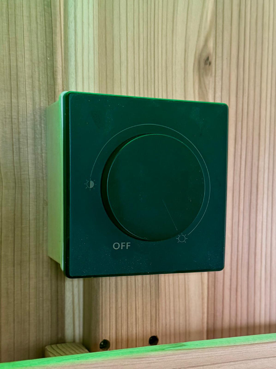 Close view of a rotary heat control mounted on a timber wall inside a Retreat sauna under green lighting.