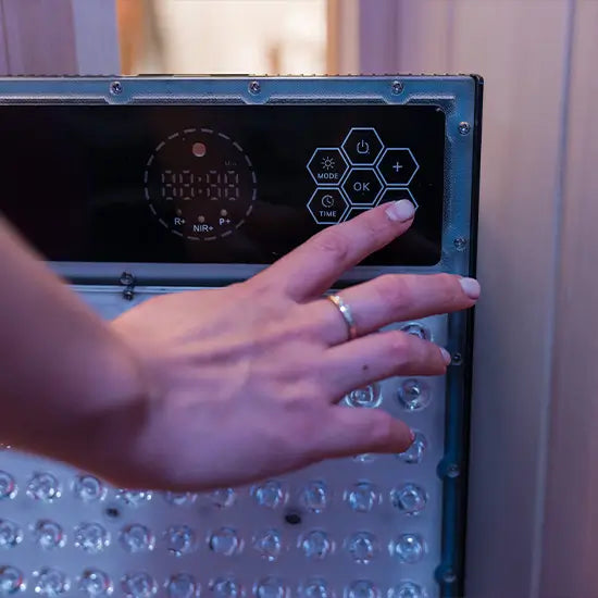 Close-up of a hand using the control buttons on a Kiva Wellness Radiance red light panel with the LEDs switched off.