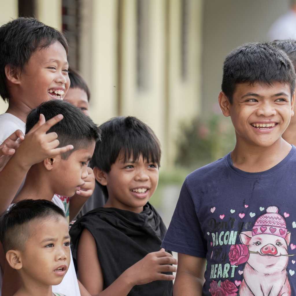 Group of children laughing together outside a yellow building.