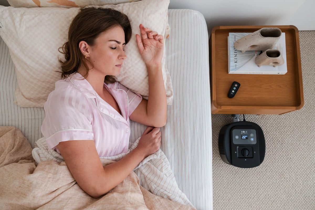 Overhead view of a woman sleeping beside a bedside table and Kiva Wellness Circadian Sleep Pod unit.