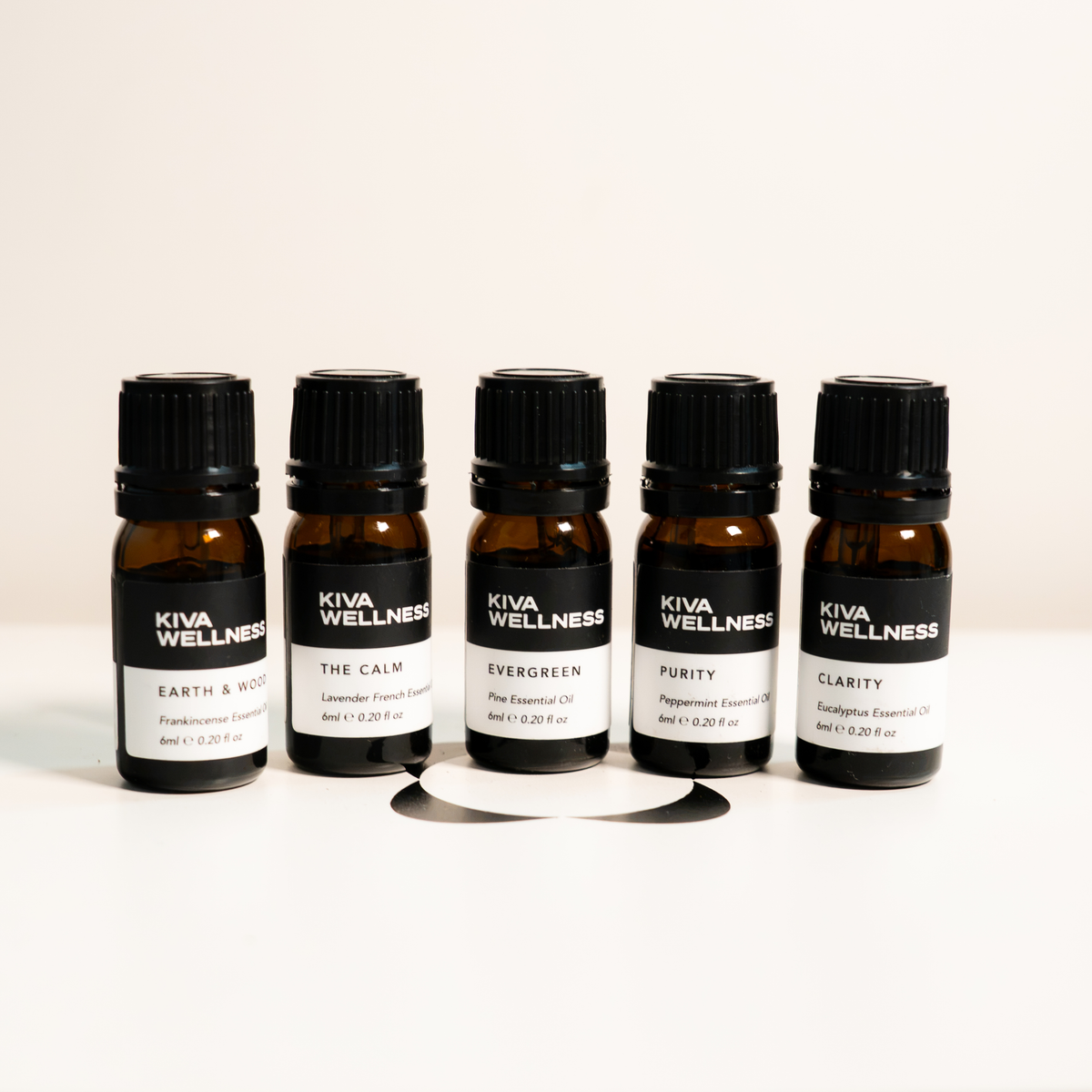 Five essential oils arranged in a row on a white surface against a light beige background.