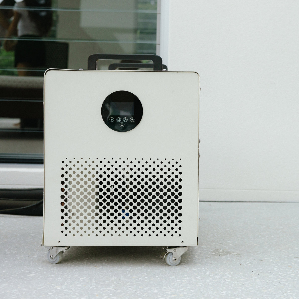 White Kiva Wellness Core ice bath chiller on wheels beside a pale exterior wall.