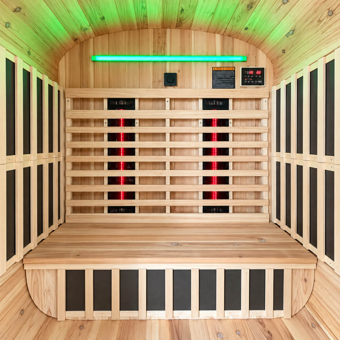 A Kiva Wellness Retreat wooden infrared sauna interior with a wooden bench, slatted back wall, side panels, green LED lighting on the ceiling, and red light tubes on the back wall.