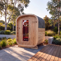 Kiva Retreat 2-3 Person outdoor full spectrum infrared sauna, situated on a stone patio beside a wooden deck in a landscaped garden setting.