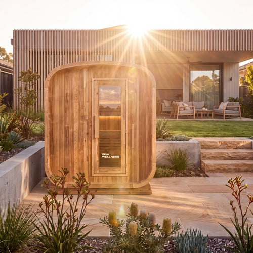 Kiva Ritual 6 Person timber front outdoor Finnish sauna stands on a stone patio in front of a modern house at sunset.