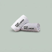 Two rolled white sauna towels displayed on a solid sage green background.