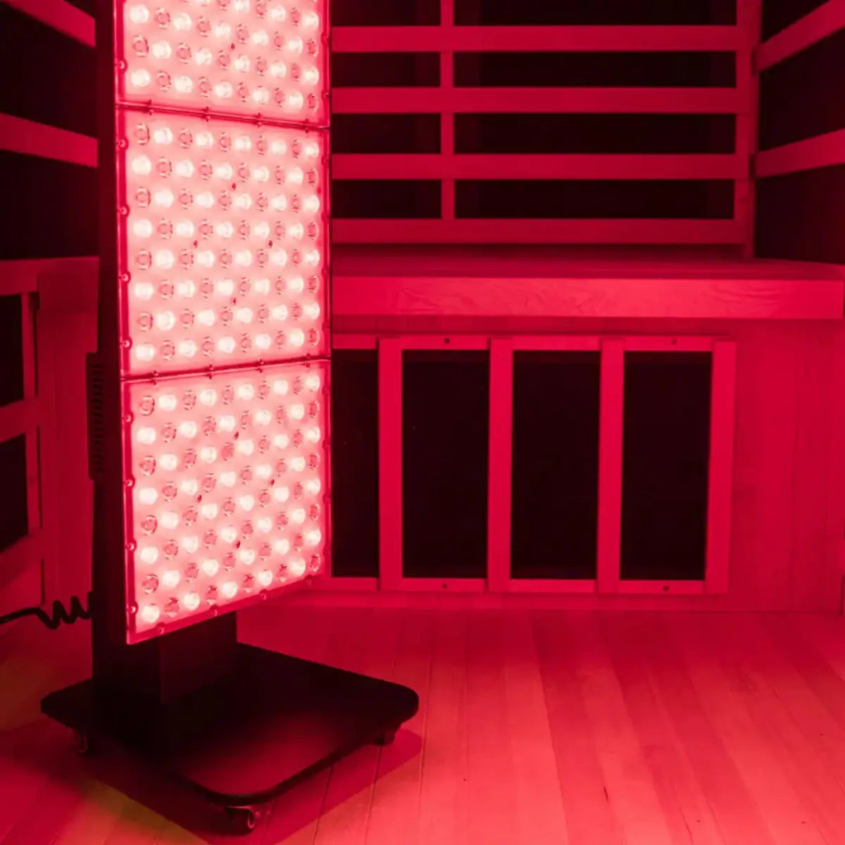 Kiva Wellness Radiance red light therapy panel glowing beside the timber bench inside an infrared sauna.