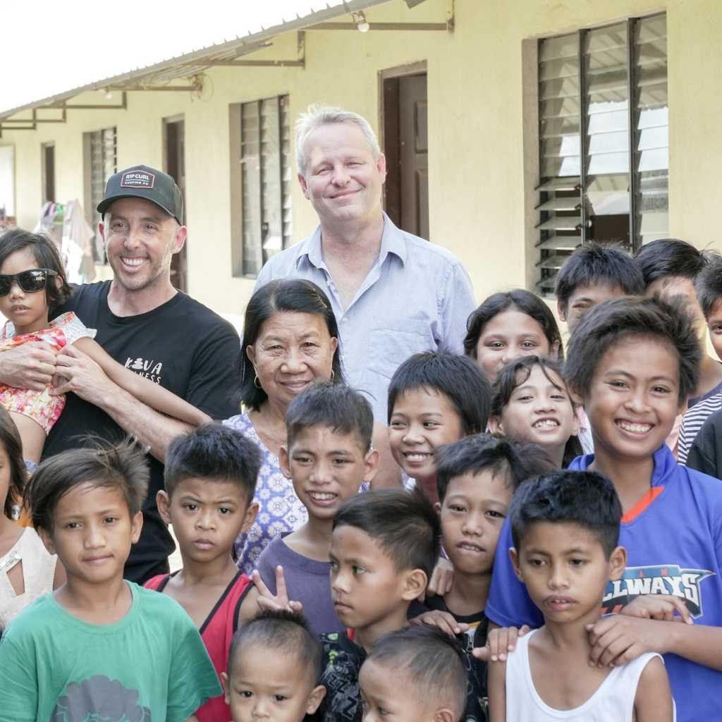 Adults and children gathered outside a pale yellow building.
